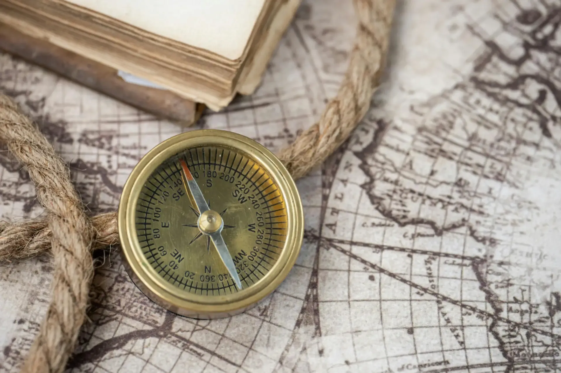 A compass and an antique book placed on a detailed map, symbolizing exploration and navigation through history.