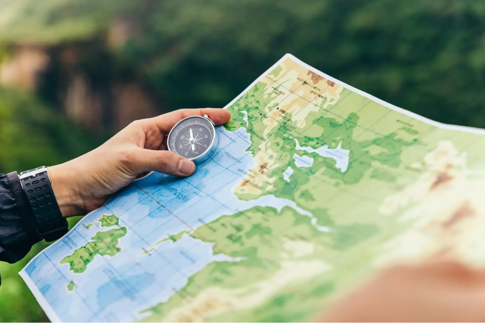 A person stands in the mountains, holding a map in one hand and a compass in the other, navigating the terrain.