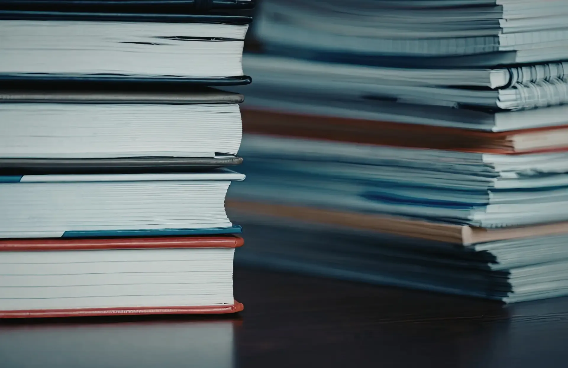 A stack of various books neatly arranged on a wooden table, showcasing colorful spines and covers.